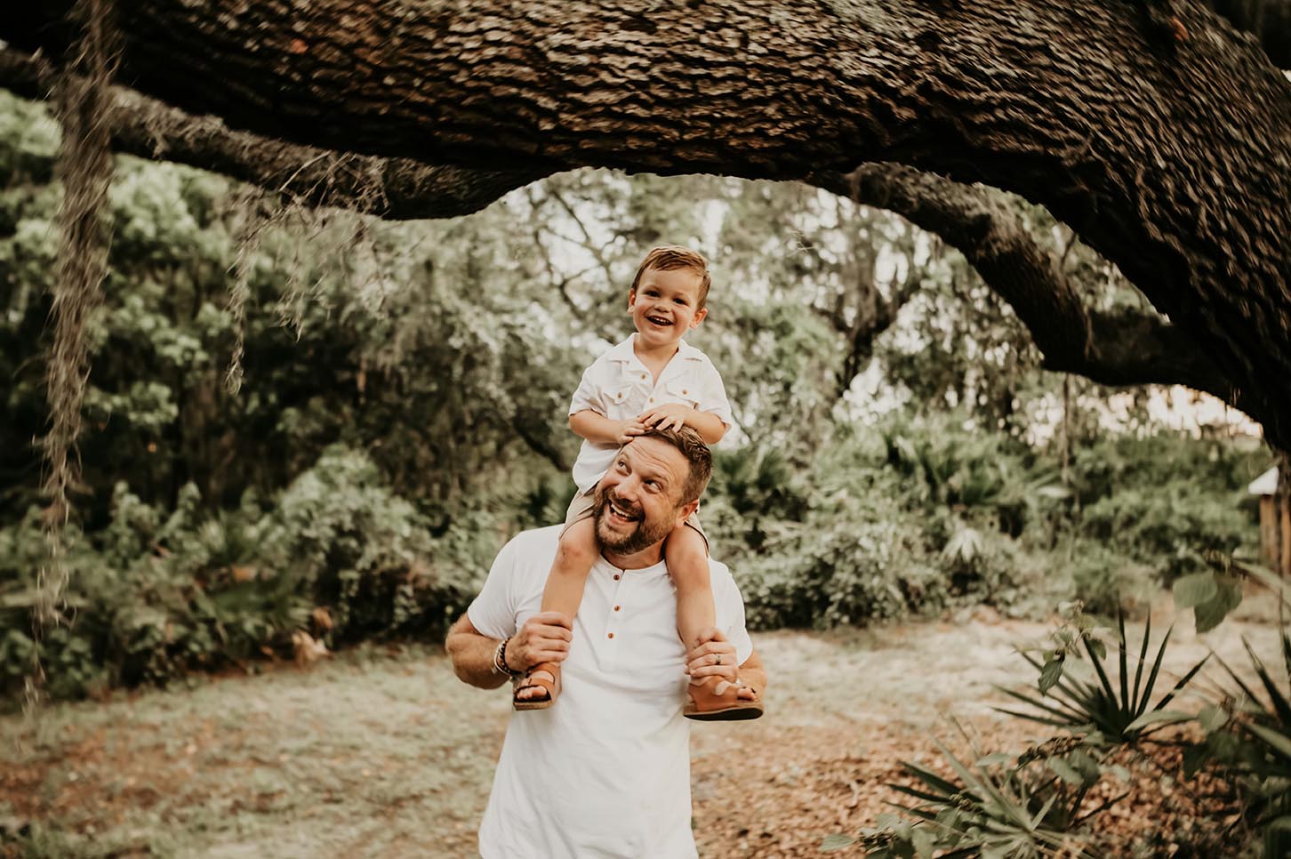 A man holding his son under a tree.
