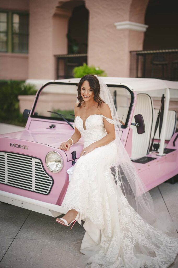 A bride is posing next to a pink jeep.