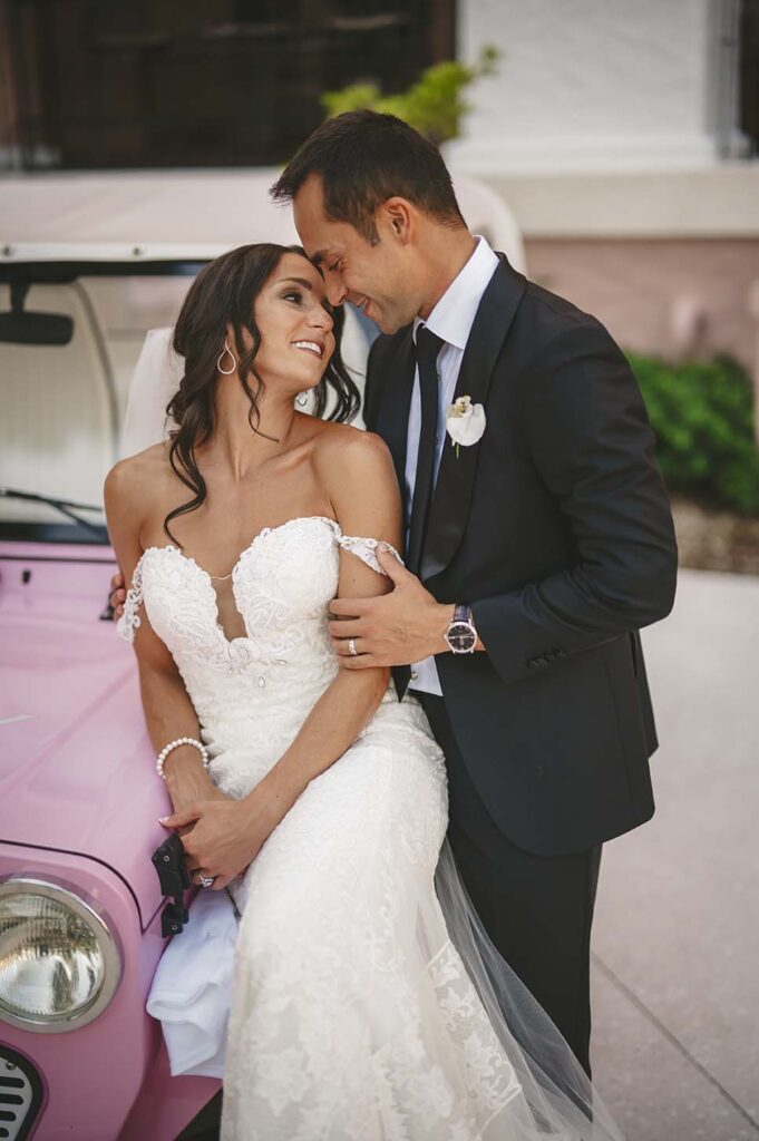 A bride and groom posing in front of a pink jeep.