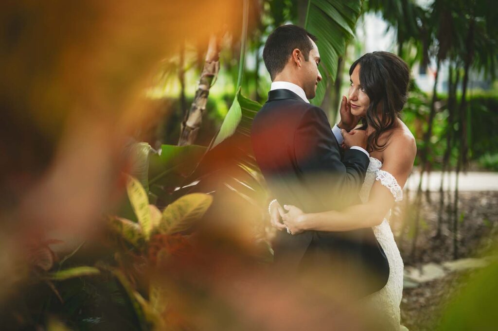 A bride and groom embrace in a tropical garden.
