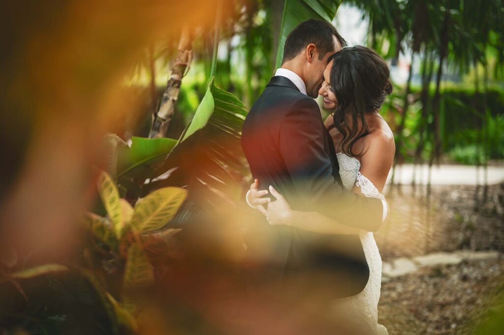 A bride and groom embrace in a tropical garden.
