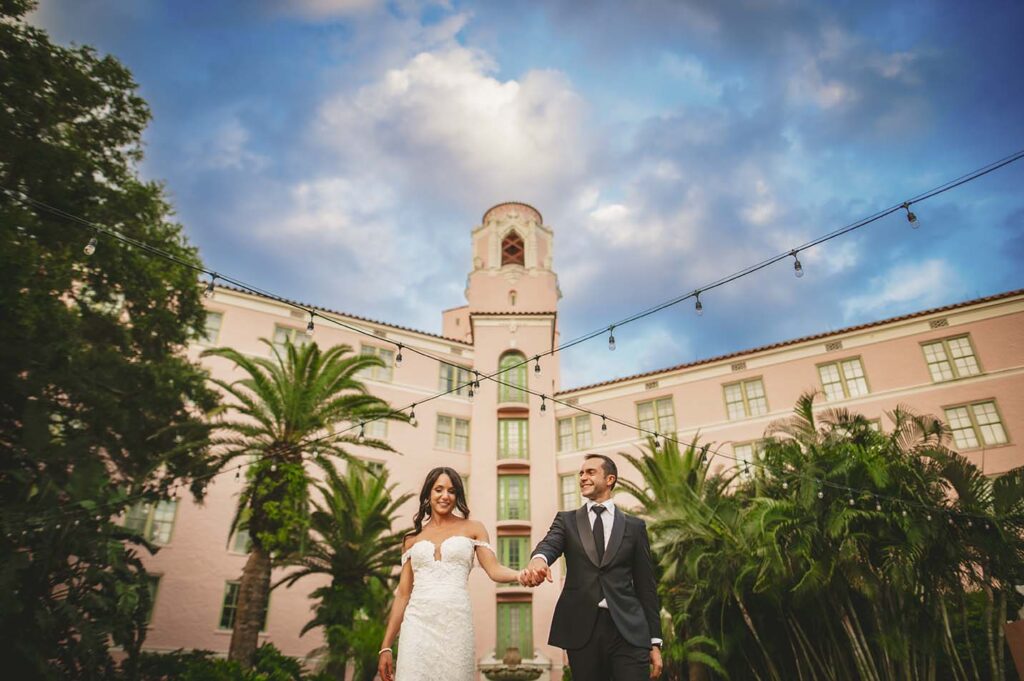 A bride and groom holding hands in front of a pink building.