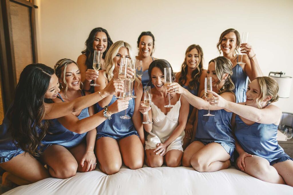A group of bridesmaids toasting champagne on a bed.