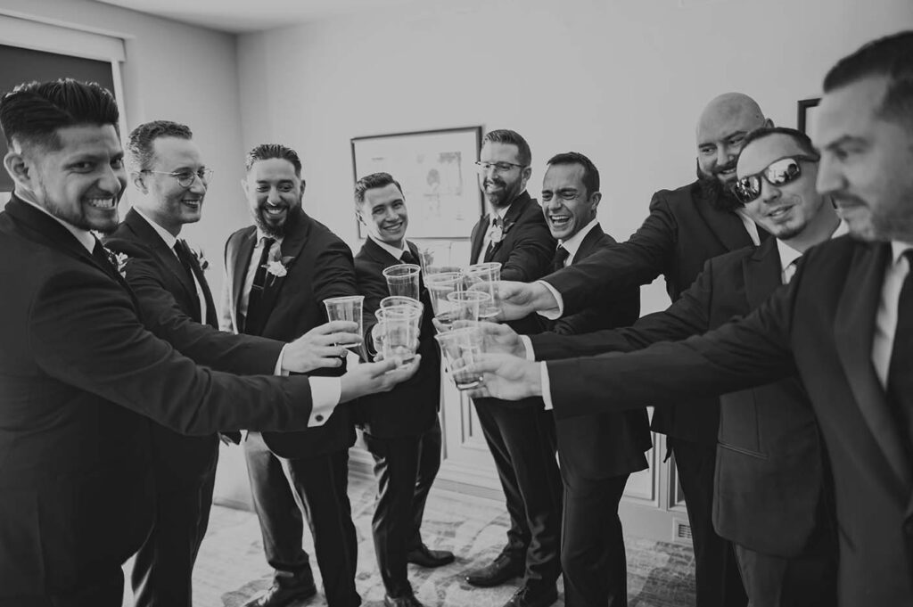 A group of groomsmen toasting in a black and white photo.