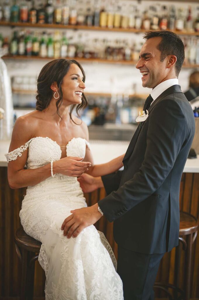 A bride and groom smiling at each other at a bar.